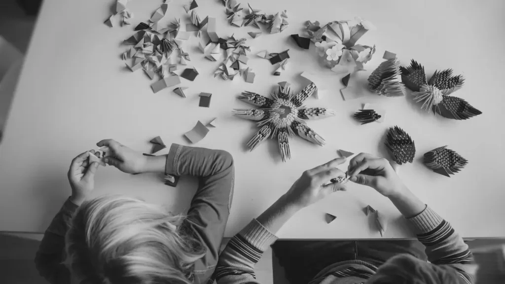 Two children sitting at a table making paper crafts, representing hands-on creative learning at home.