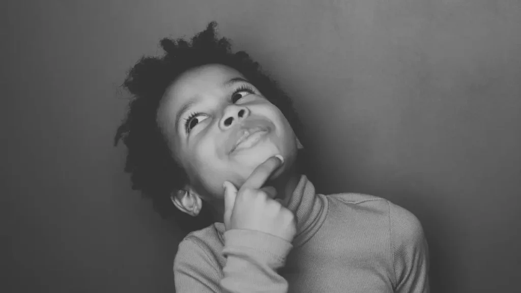 Child looking upwards thoughtfully with hand on chin, representing curiosity and reflection in learning.