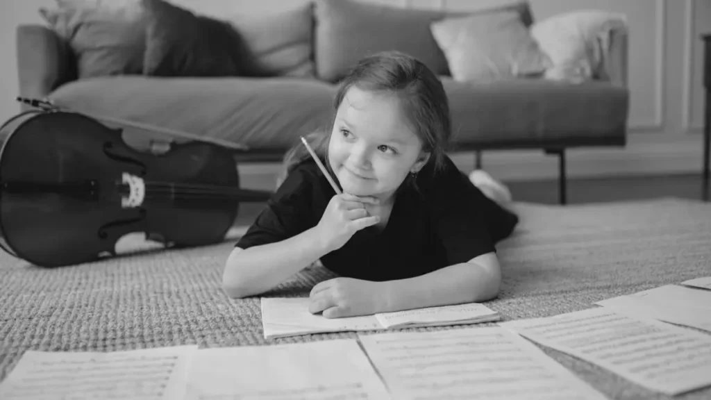Young child lying on the floor and writing in a notebook with learning materials spread out nearby.