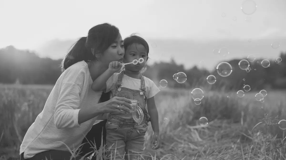 Parent and young child blowing bubbles together outdoors, representing playful learning, connection, and confidence-building in home education.