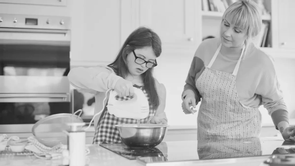 Parent smiling at a young child sitting on a kitchen counter, representing everyday learning, connection, and home education routines.