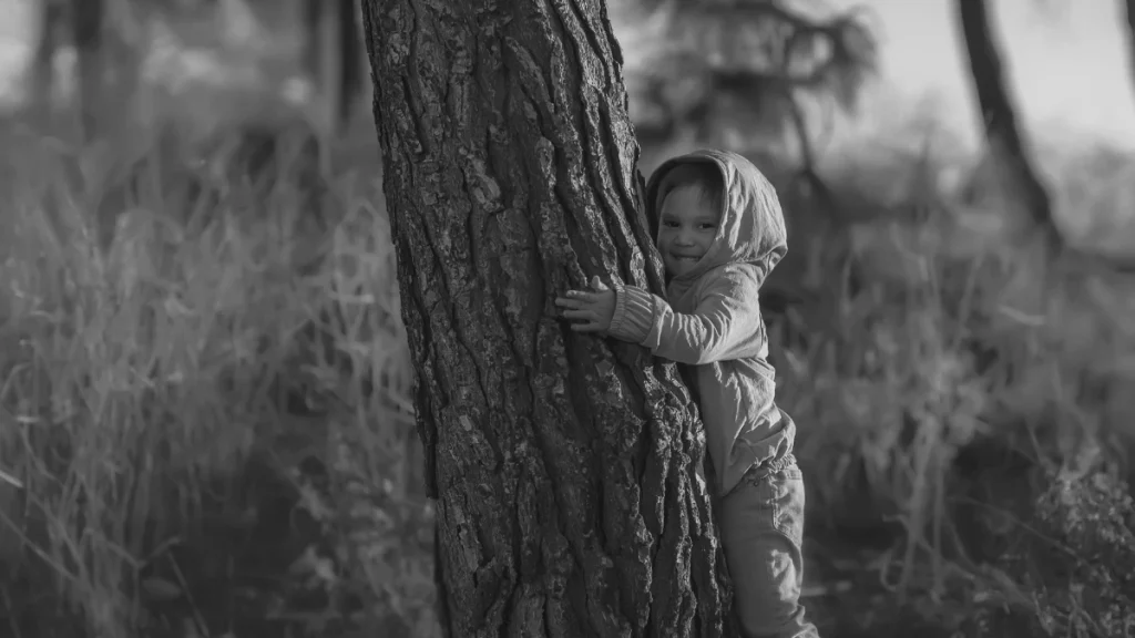 Young child hugging a tree outdoors, representing play, regulation, and reconnecting with nature during deschooling.
