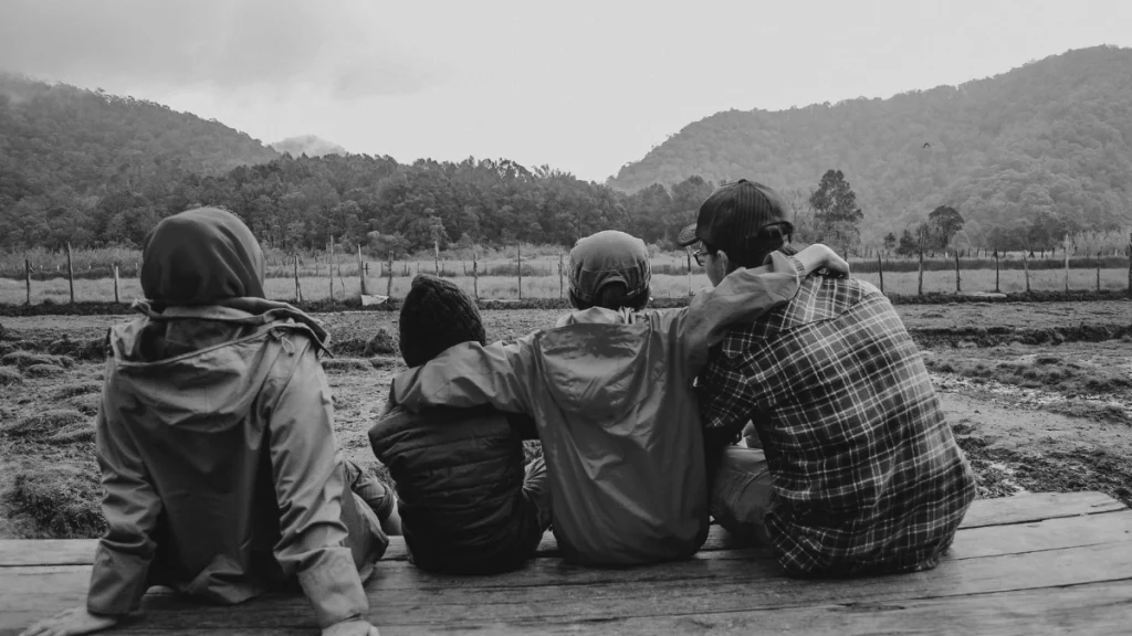 Family sitting together outdoors looking at the landscape, representing connection, reflection, and slowing down during deschooling.