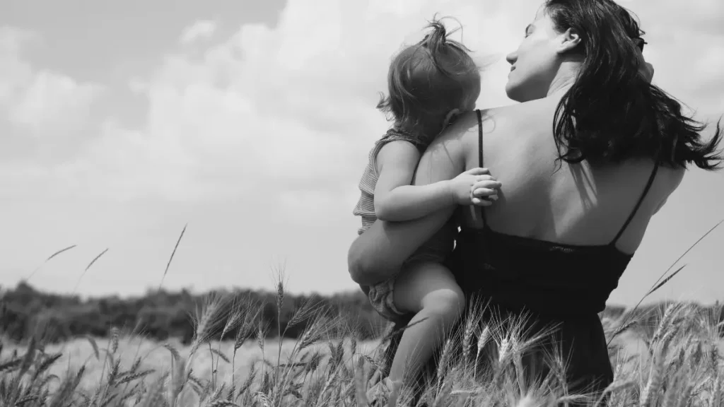 Parent holding a small child in a grassy field, representing wellbeing, freedom, and a gentle home education journey.