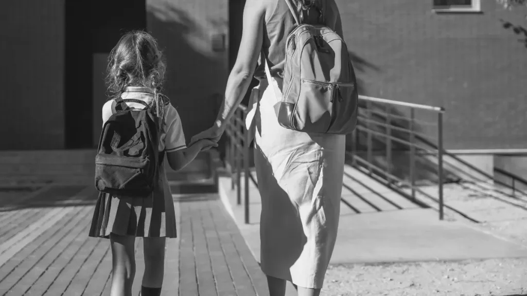 Parent holding a child’s hand while walking them towards school, representing school anxiety and difficult school mornings.