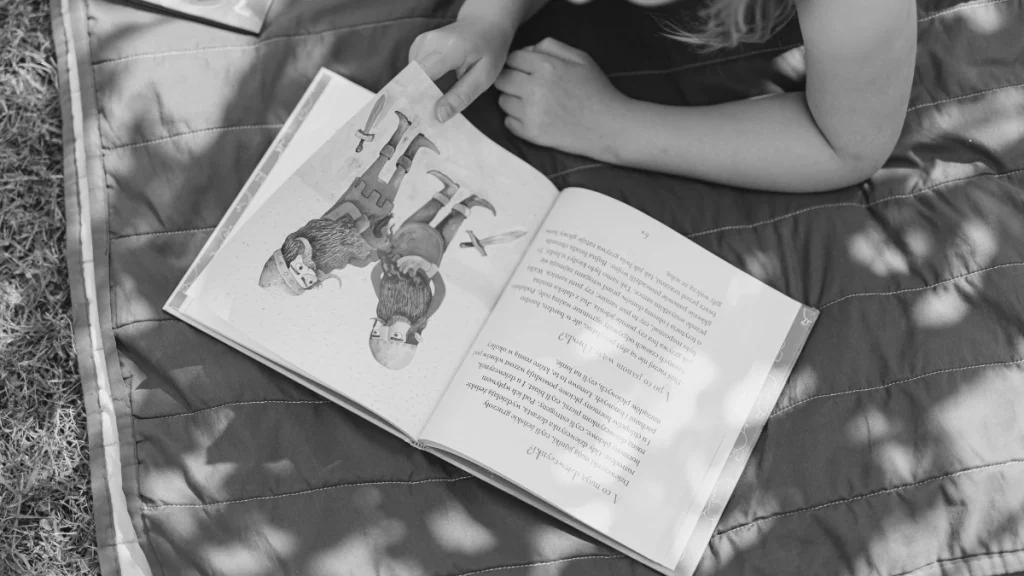 Open children’s book on a picnic blanket outdoors, representing flexible learning through books in home education.