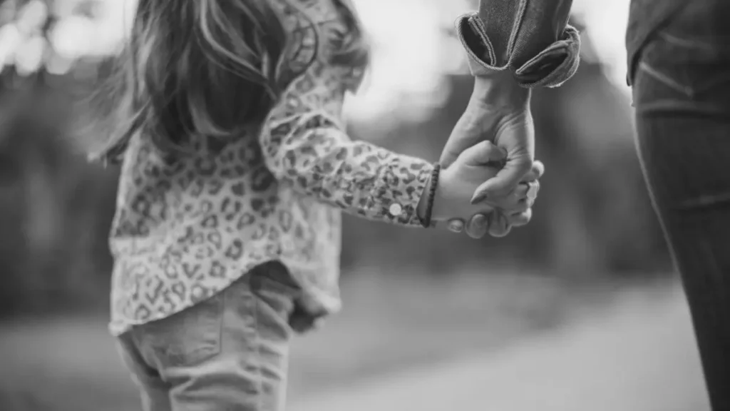 Parent holding a child’s hand outdoors, representing guidance, trust and emotional support in home education.