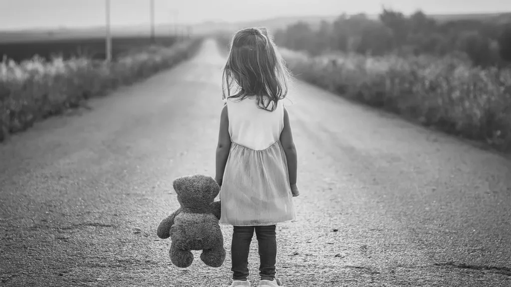 Young child holding a teddy bear on a quiet road, representing home education as a different learning path for children and families.