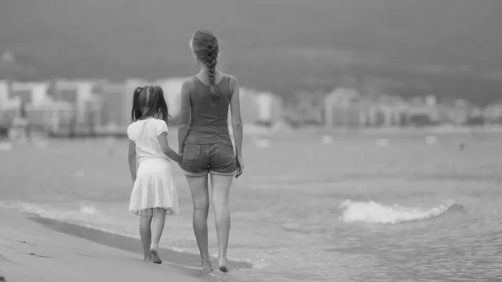 Parent and child walking hand in hand along the beach, representing lifestyle changes and moving for a better environment or education options.