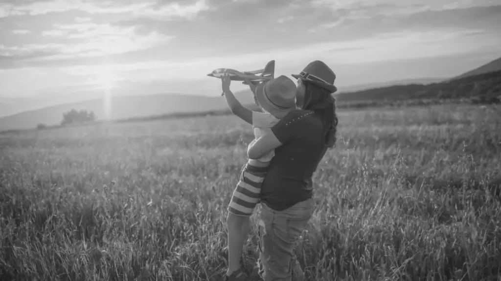 Parent holding a child in a field as they play with a toy aeroplane, representing imagination, freedom, and future-focused home education.