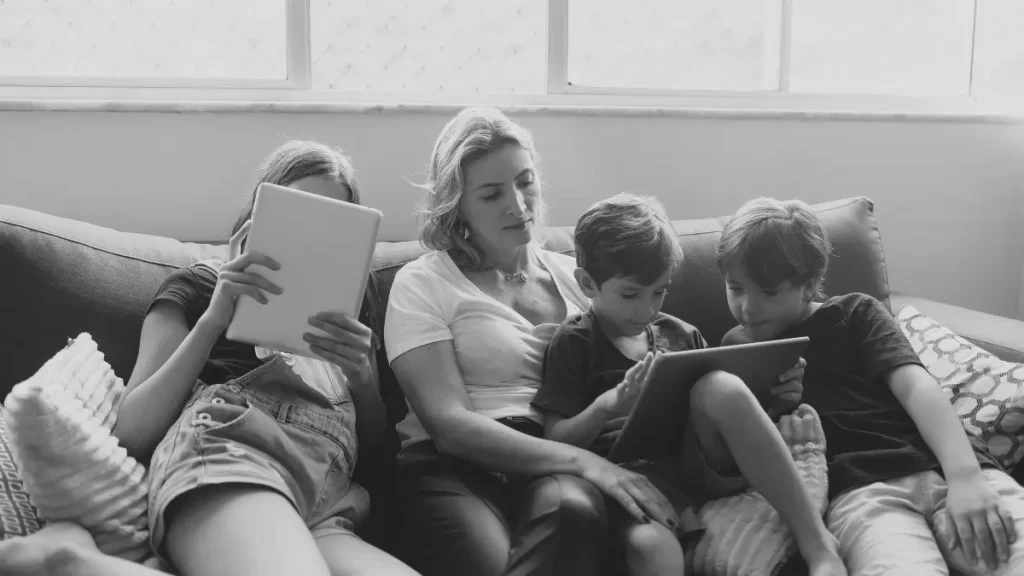 Children using tablets at home with a parent nearby, showing digital learning in home education.