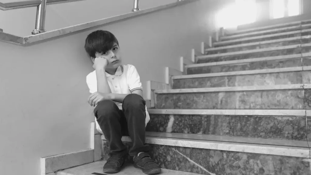 Child sitting alone on school stairs looking unhappy, representing children who may struggle in traditional school settings.