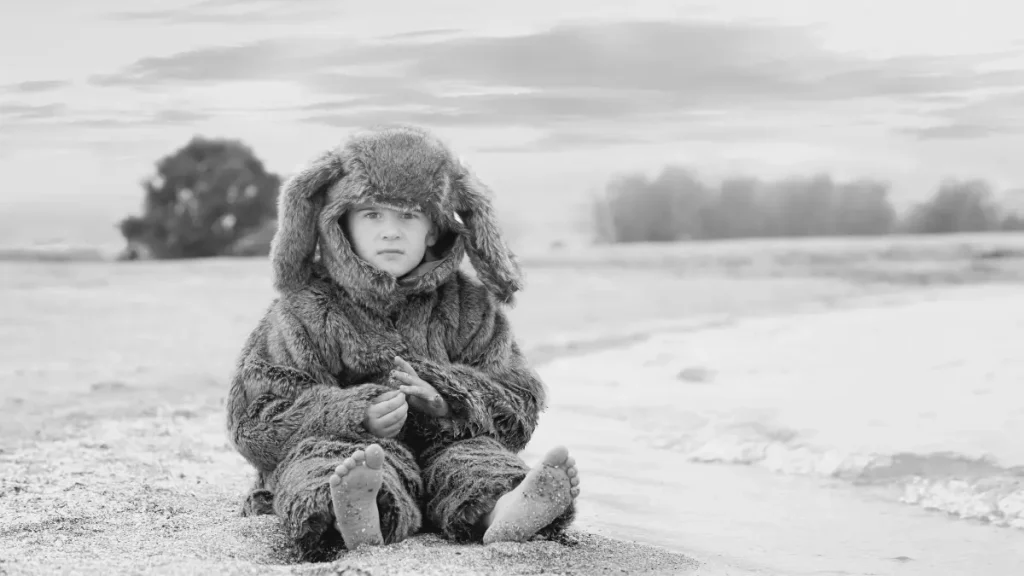 Child sitting on a beach in a warm costume, representing play, imagination and real-world learning in home education.