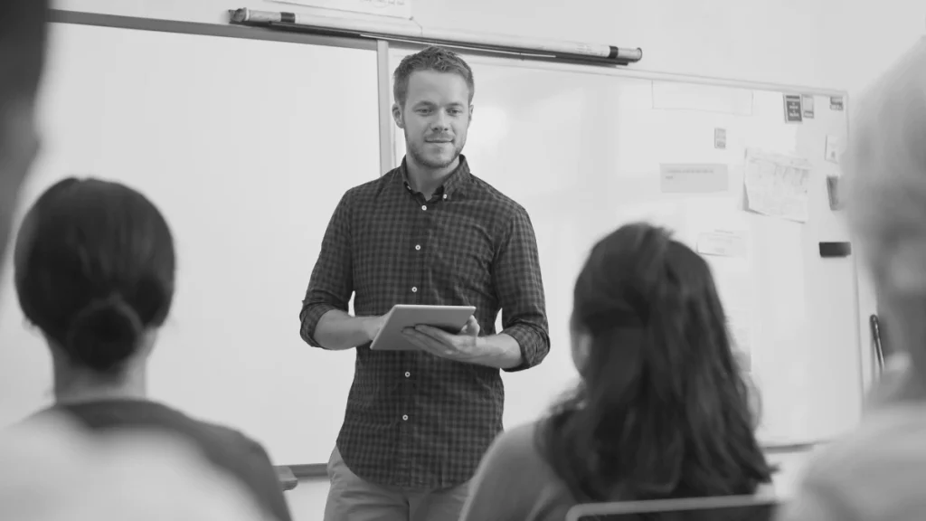 Teacher standing at the front of a classroom with pupils seated, representing the idea that teachers learn on the job too.