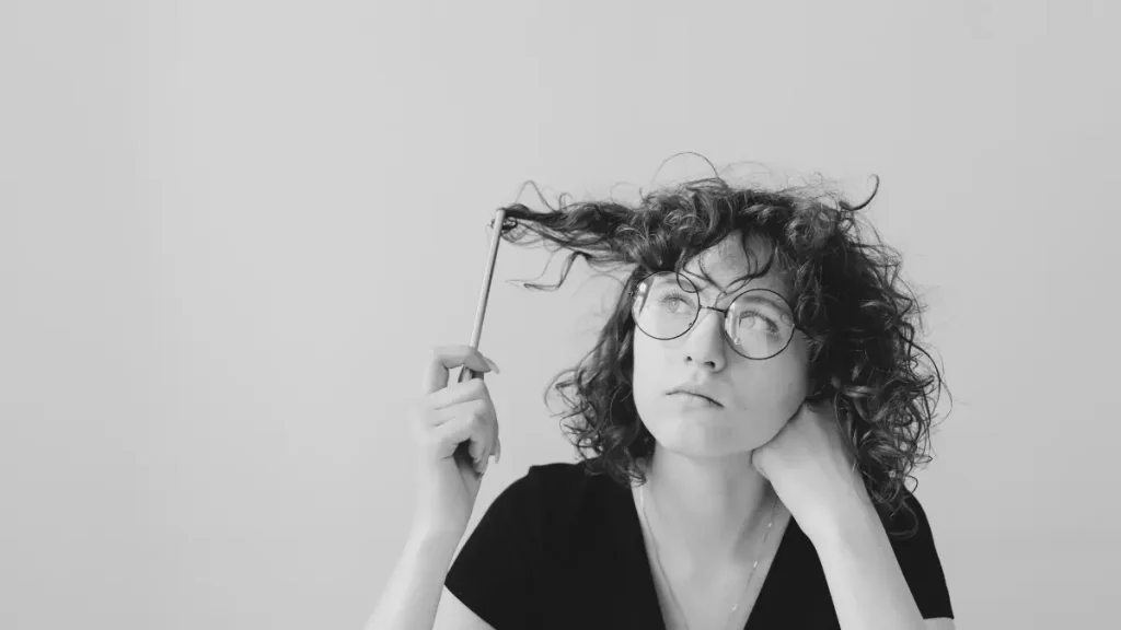 Thoughtful adult holding a pencil and looking upwards, representing the mental load of deciding between school and home education.